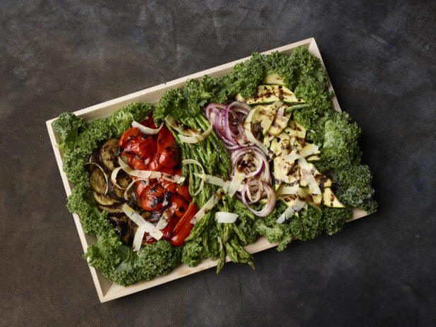 Over head of grilled vegetable platter in a wooden tray on a dark background