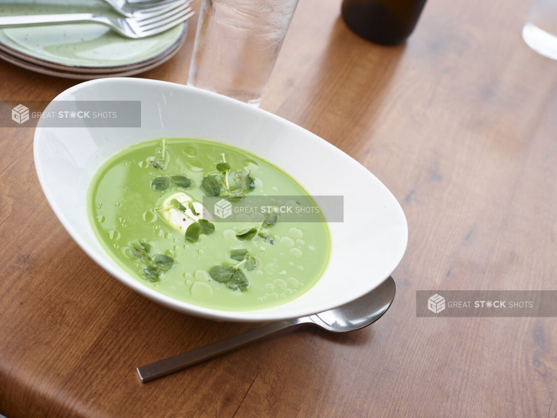 Large white bowl of spring pea soup garnished with pea shoots and cream dollop