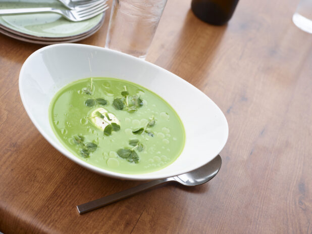 Large white bowl of spring pea soup garnished with pea shoots and cream dollop