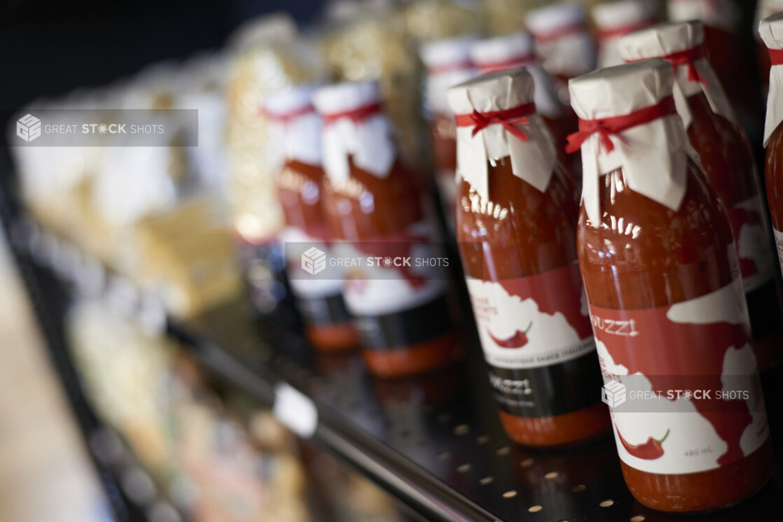 Bottles of red sauce with paper covers tied over the lids, tilted angle, close-up