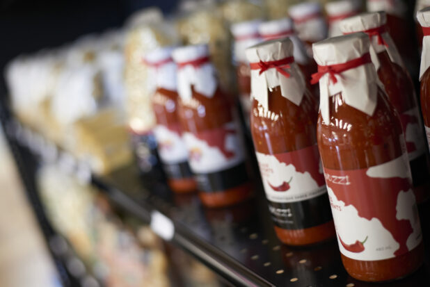 Bottles of red sauce with paper covers tied over the lids, tilted angle, close-up