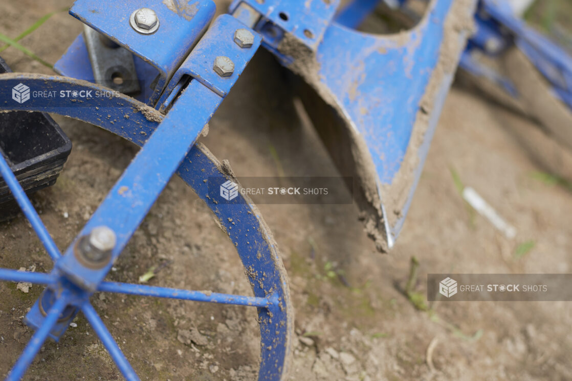 Close Up of a Blue Painted Metal Wheel Hoe or Cultivator Farming Equipment on the Ground in an Outdoor Farm Setting