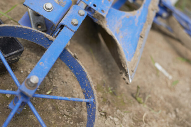 Close Up of a Blue Painted Metal Wheel Hoe or Cultivator Farming Equipment on the Ground in an Outdoor Farm Setting