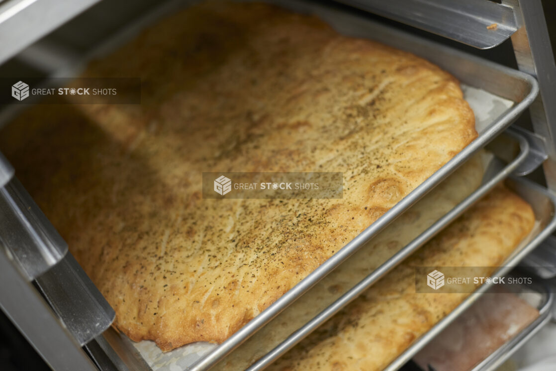 Close Up of Full Sized Sheet Pan Herbed Focaccia Bread Resting in a Cooling Rack in the Kitchen of a Gourmet Grocery Store