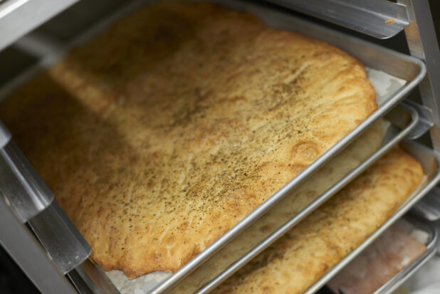 Close Up of Full Sized Sheet Pan Herbed Focaccia Bread Resting in a Cooling Rack in the Kitchen of a Gourmet Grocery Store