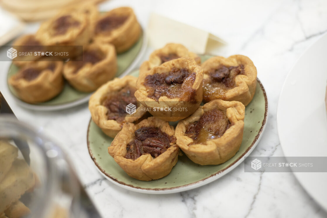 A Stack of Freshly Baked Butter Pecan Tarts on a Green Ceramic Dish on a Marble Counter Top in a Gourmet Grocery Store Setting