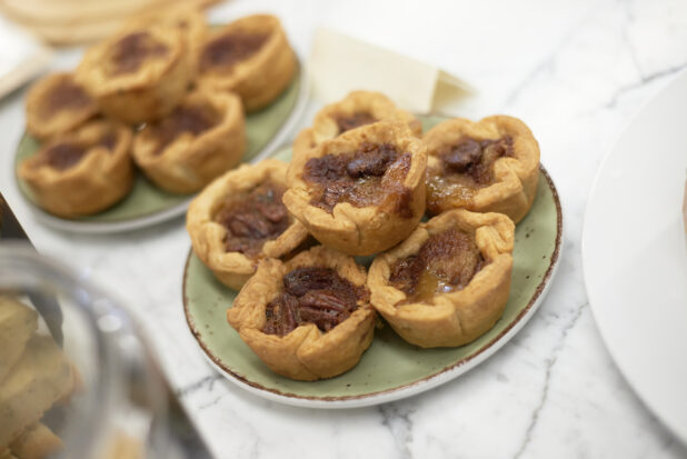 A Stack of Freshly Baked Butter Pecan Tarts on a Green Ceramic Dish on a Marble Counter Top in a Gourmet Grocery Store Setting