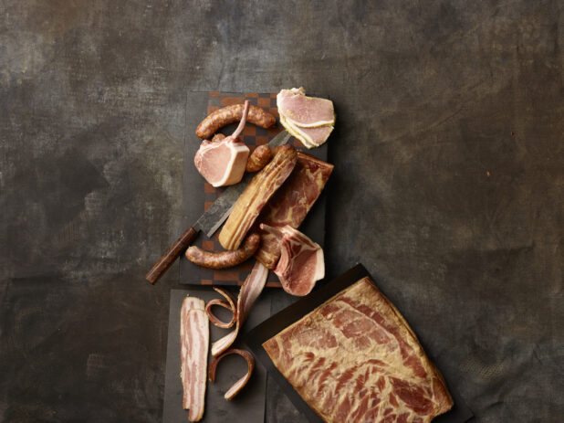 A variety of fresh and cured meats on a dark grey background