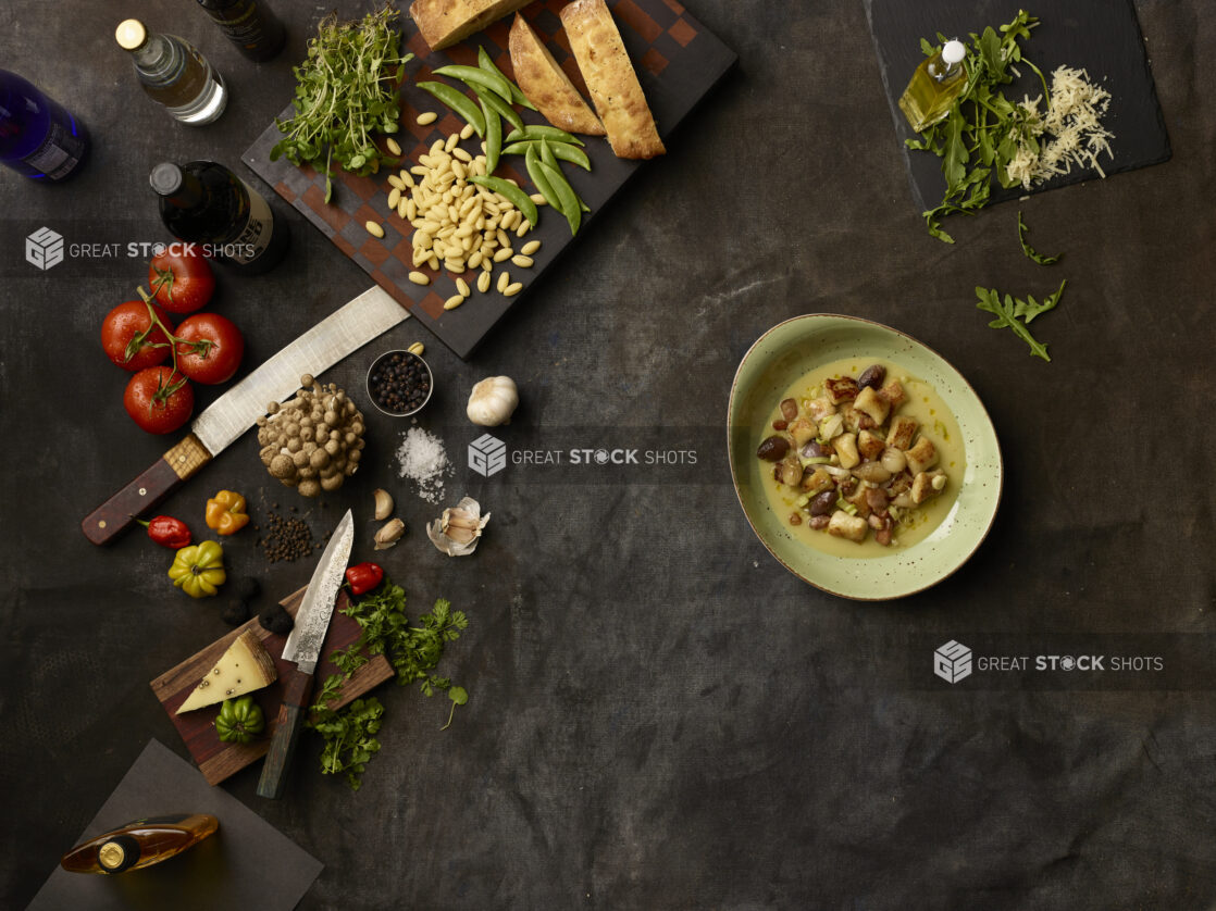 Bowl of gnocchi and many fresh ingredients on a dark grey cloth background