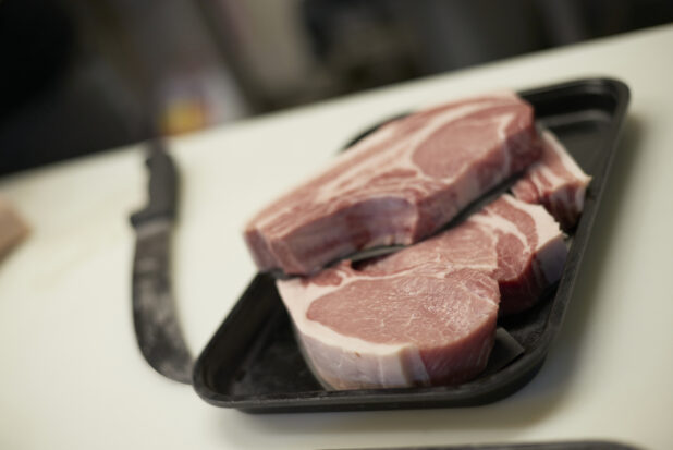 Close Up of Fresh-Cut Centre Pork Loin Chops on a Black Plastic Tray in a Butcher's Kitchen Setting