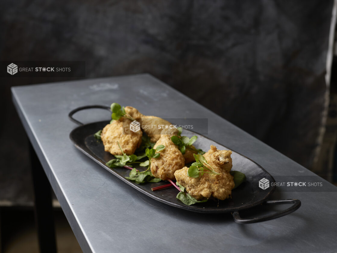 Black serving platter of fried tuscan chicken garnished with greens on a metal table