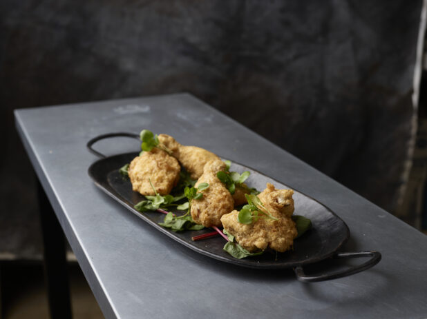 Black serving platter of fried tuscan chicken garnished with greens on a metal table