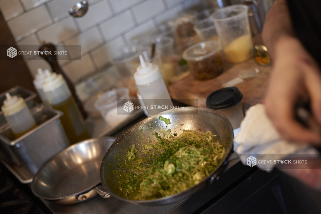 Chef Cooking Stir Fry Noodles with Vegetables in a Stainless Steel Frying Pan in a Commercial Kitchen Setting of a Gourmet Grocery Store