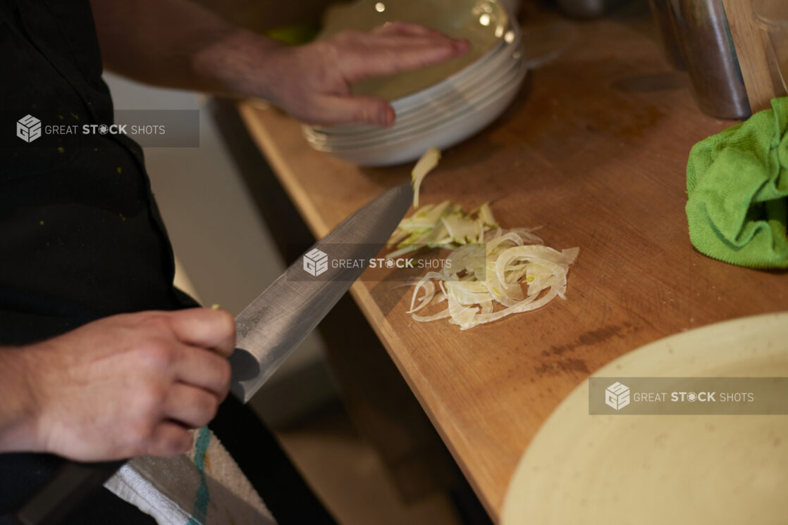 A chef's hand holding a knife over some thinly sliced onions