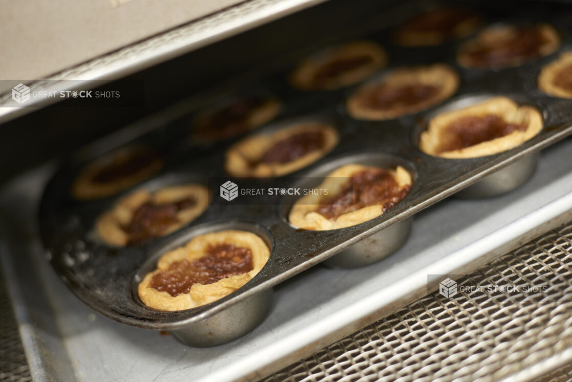 Freshly Baked Butter Pecan Tarts in a Muffin Baking Tin Coming Out of an Oven in a Gourmet Grocery Store Kitchen Setting