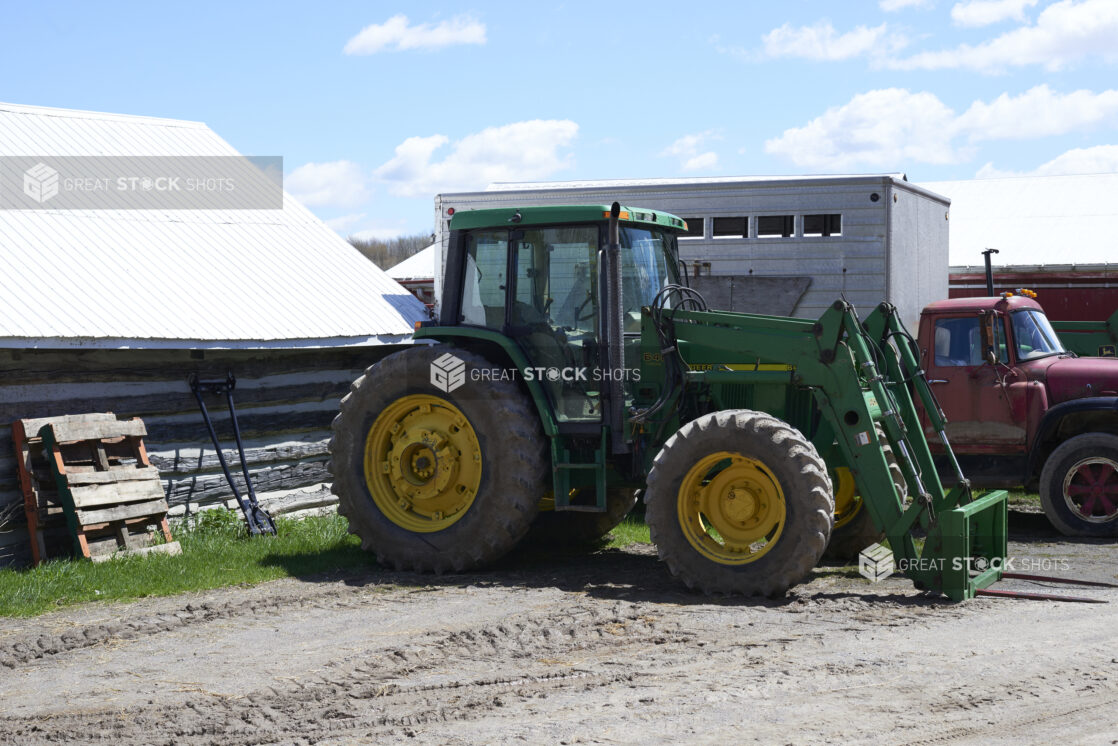 Large Green John Deere Tractor and Red Farm Truck Parked on an Unpaved Dirt Lot on a Farm Setting