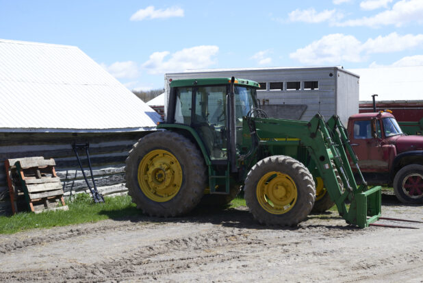 Large Green John Deere Tractor and Red Farm Truck Parked on an Unpaved Dirt Lot on a Farm Setting