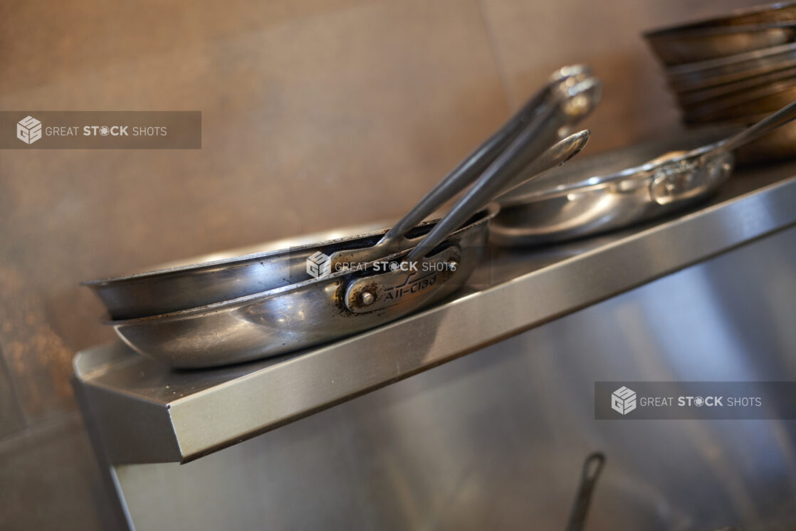 Sautée pans stacked on a steel shelf above a kitchen range, close-up