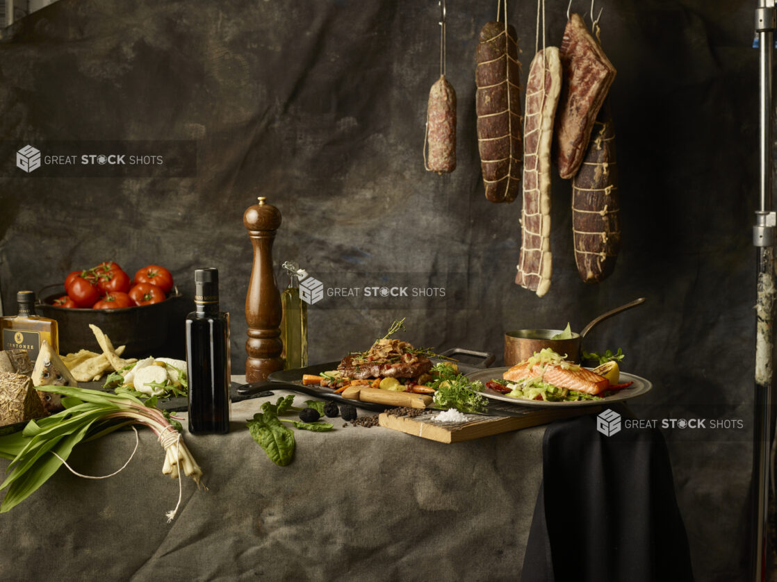 Long table with entrees and quality ingredients with hanging meat in the background with a dark backdrop