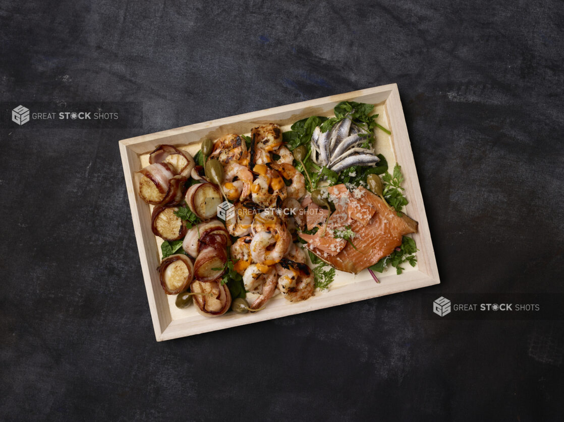 Overhead view of a seafood platter on a wooden tray with a dark background