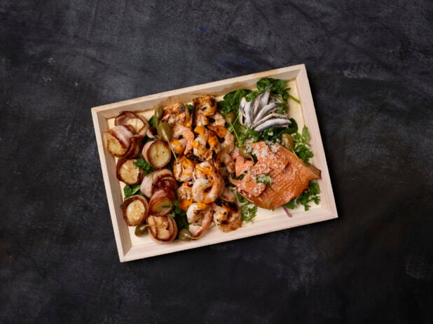 Overhead view of a seafood platter on a wooden tray with a dark background
