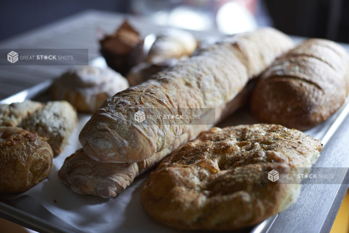 A Baking Sheet of Freshly Baked Breads, Baguettes, Focaccia and Pastries on a Stainless Steel Counter in a Gourmet Grocery Store Interior