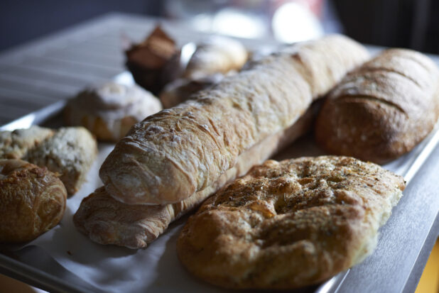 A Baking Sheet of Freshly Baked Breads, Baguettes, Focaccia and Pastries on a Stainless Steel Counter in a Gourmet Grocery Store Interior