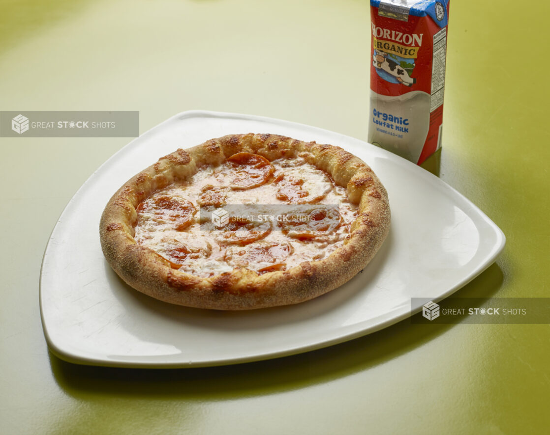 Kids meal of uncut pepperoni pizza with drink box of milk on a green background