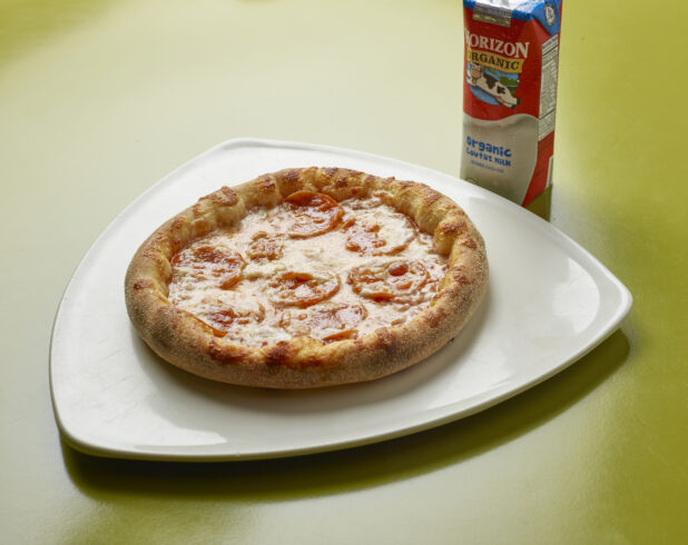 Kids meal of uncut pepperoni pizza with drink box of milk on a green background