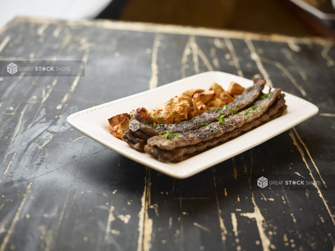 A White Ceramic Platter of Middle Eastern Beef and Chicken Kebabs for Catering on a Black Painted Weathered Wood Table