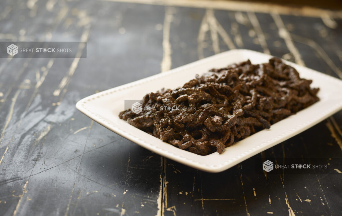 A White Ceramic Platter of Middle Eastern Beef Shawarma for Catering on a Black Painted Weathered Wood Table