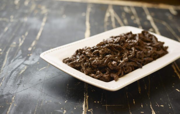 A White Ceramic Platter of Middle Eastern Beef Shawarma for Catering on a Black Painted Weathered Wood Table