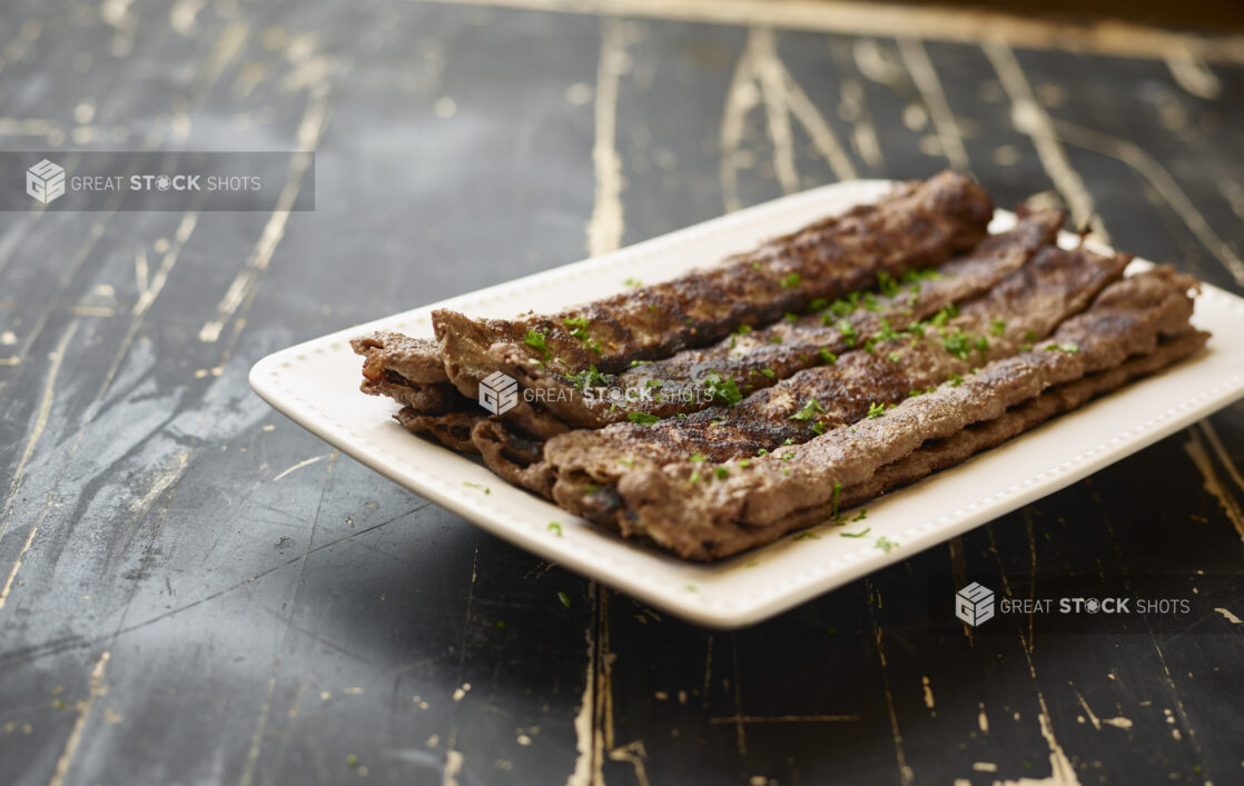 A White Ceramic Platter of Middle Eastern Beef Kebabs for Catering on a Black Painted Weathered Wood Table