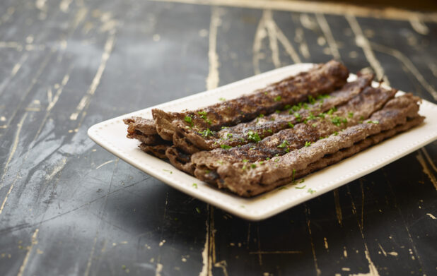 A White Ceramic Platter of Middle Eastern Beef Kebabs for Catering on a Black Painted Weathered Wood Table