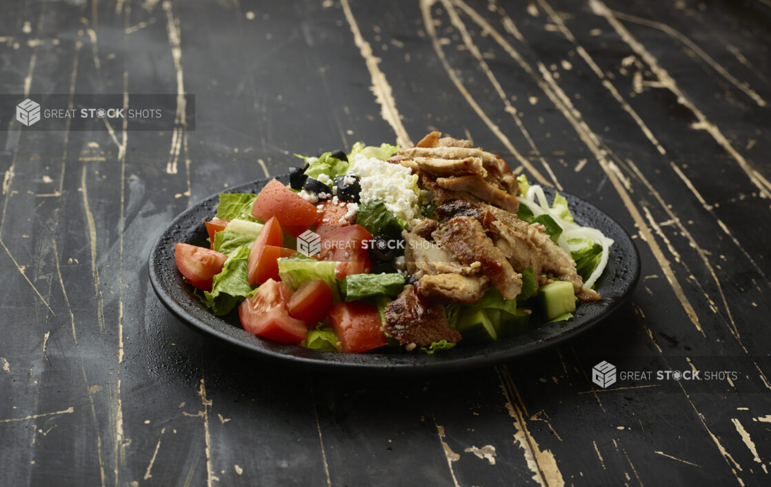 Greek Salad with Chicken Shawarma on a Black Ceramic Plate on a Black Painted Weathered Wooden Table