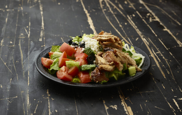 Greek Salad with Chicken Shawarma on a Black Ceramic Plate on a Black Painted Weathered Wooden Table
