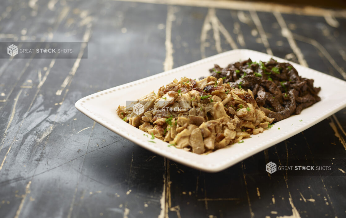 A White Ceramic Platter of Middle Eastern Beef and Chicken Shawarma for Catering on a Black Painted Weathered Wood Table