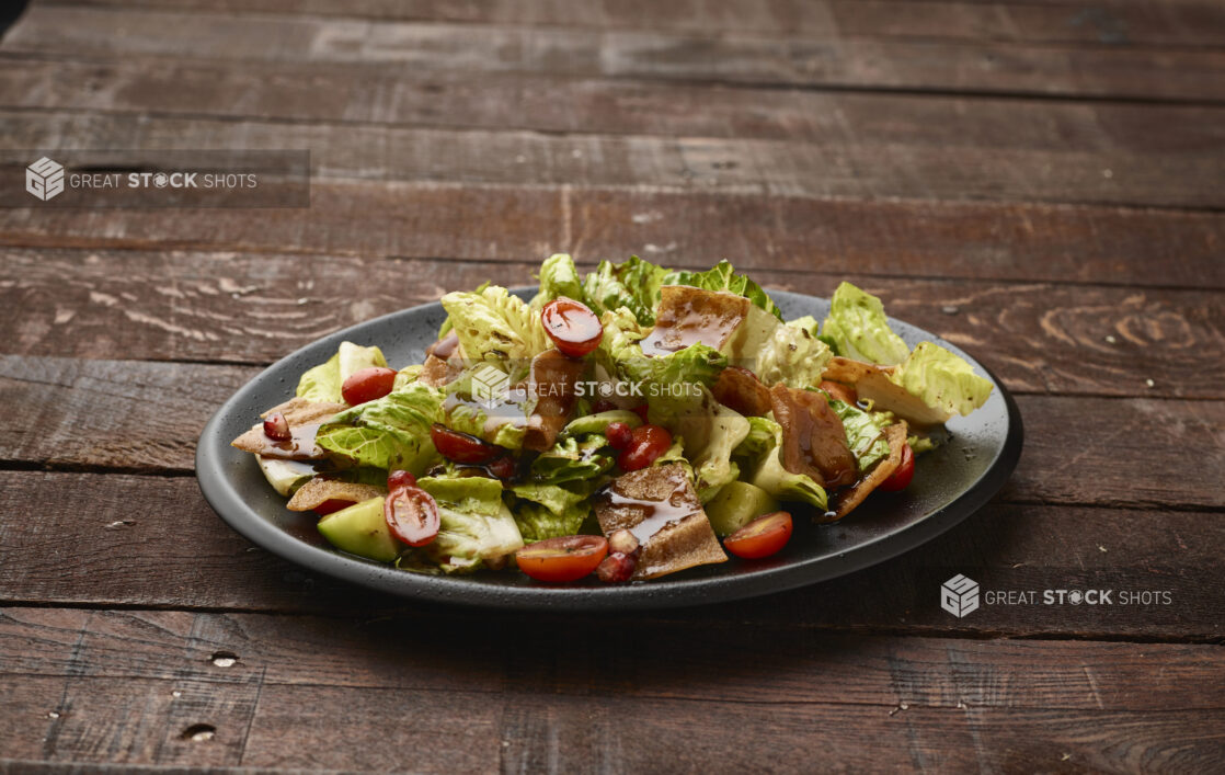 Garden Salad with Gyro Meat and Balsamic Vinaigrette Drizzle on a Black Ceramic Dish on a Dark Wood Panelled Table