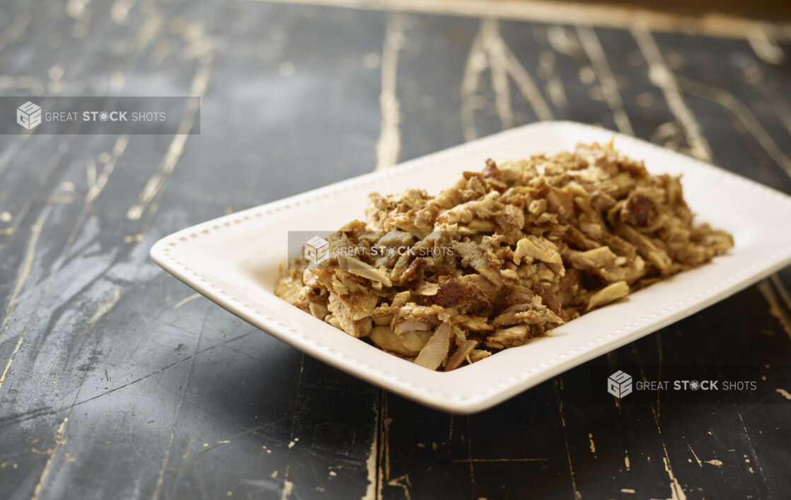 A White Ceramic Platter of Middle Eastern Chicken Shawarma for Catering on a Black Painted Weathered Wood Table