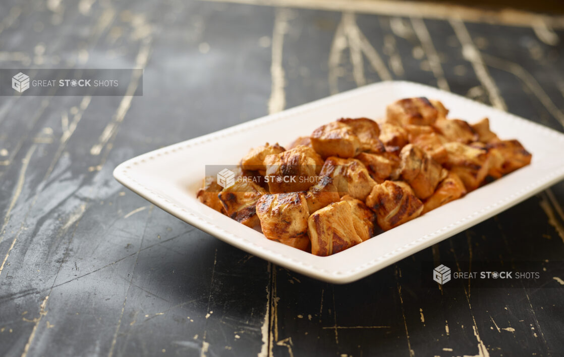 A White Ceramic Platter of Middle Eastern Chicken Kebabs for Catering on a Black Painted Weathered Wood Table