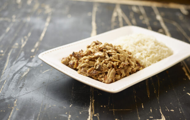A White Ceramic Platter of Middle Eastern Chicken Shawarma and White Rice on a Black Painted Weathered Wood Table