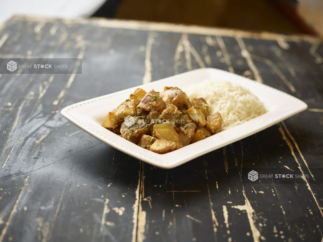 A White Ceramic Platter of Garlic Potatoes and White Rice, a Side Dish for Catering, on a Black Painted Weathered Wood Table