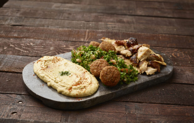 Sharing Plate: Tabbouleh, Hummus, Falafel Balls and Chicken Shawarma on a Black Slate Platter on a Dark Wood Panelled Table