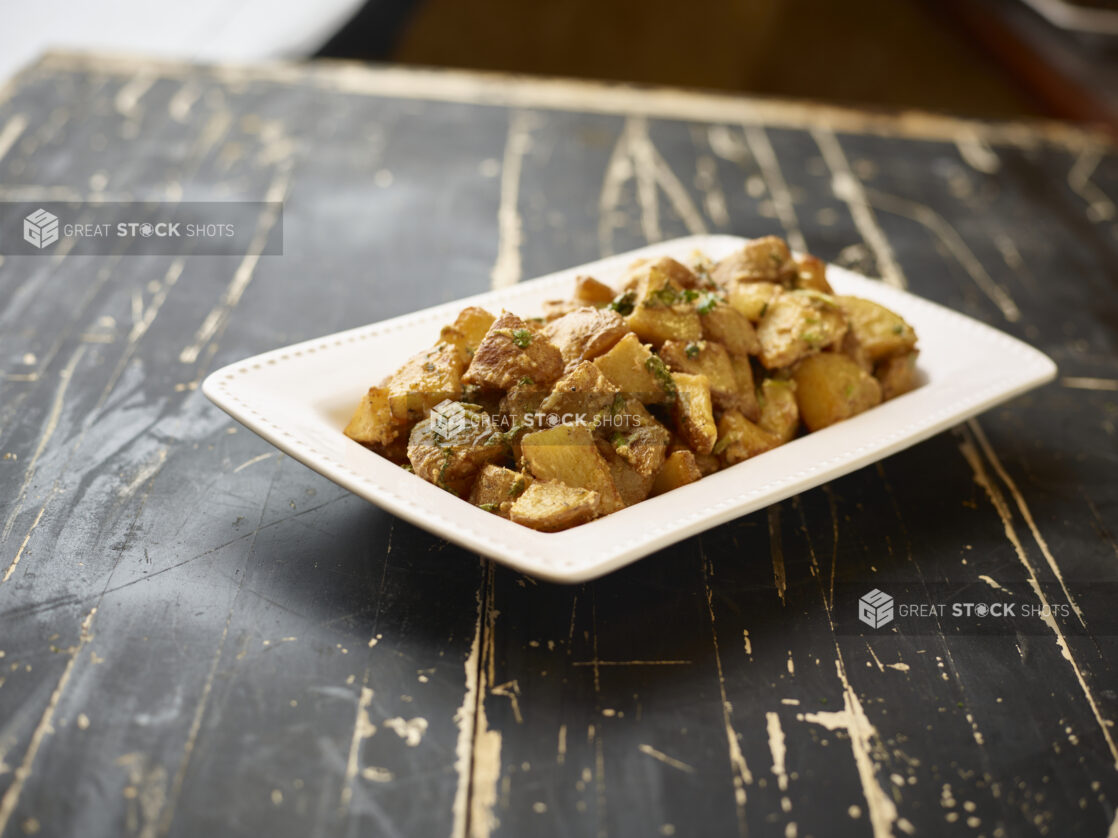 A White Ceramic Platter of Garlic Potatoes, a Side Dish for Catering, on a Black Painted Weathered Wood Table