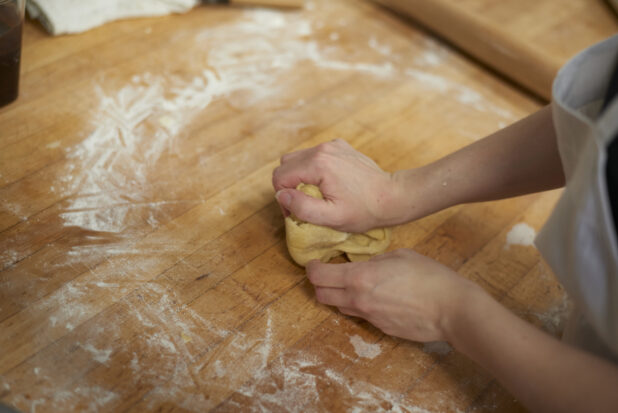 Baker kneading dough on floured wood surface