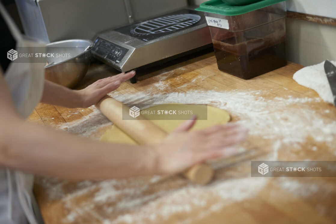 Baker rolling out dough on a floured wood board in a commercial bakery