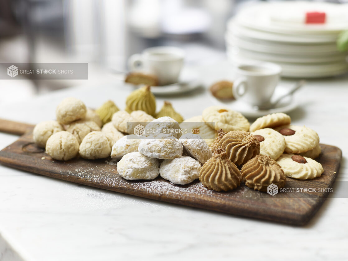 Assorted Italian Butter Cookies on a Wooden Platter Board with Espresso Coffee in Ceramic Cups on a Marble Surface