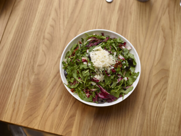 Chopped Leafy Vegetable Salad with Baby Arugula, Radicchio and Spring Mix in a Round White Ceramic Salad Bowl on a Wooden Table