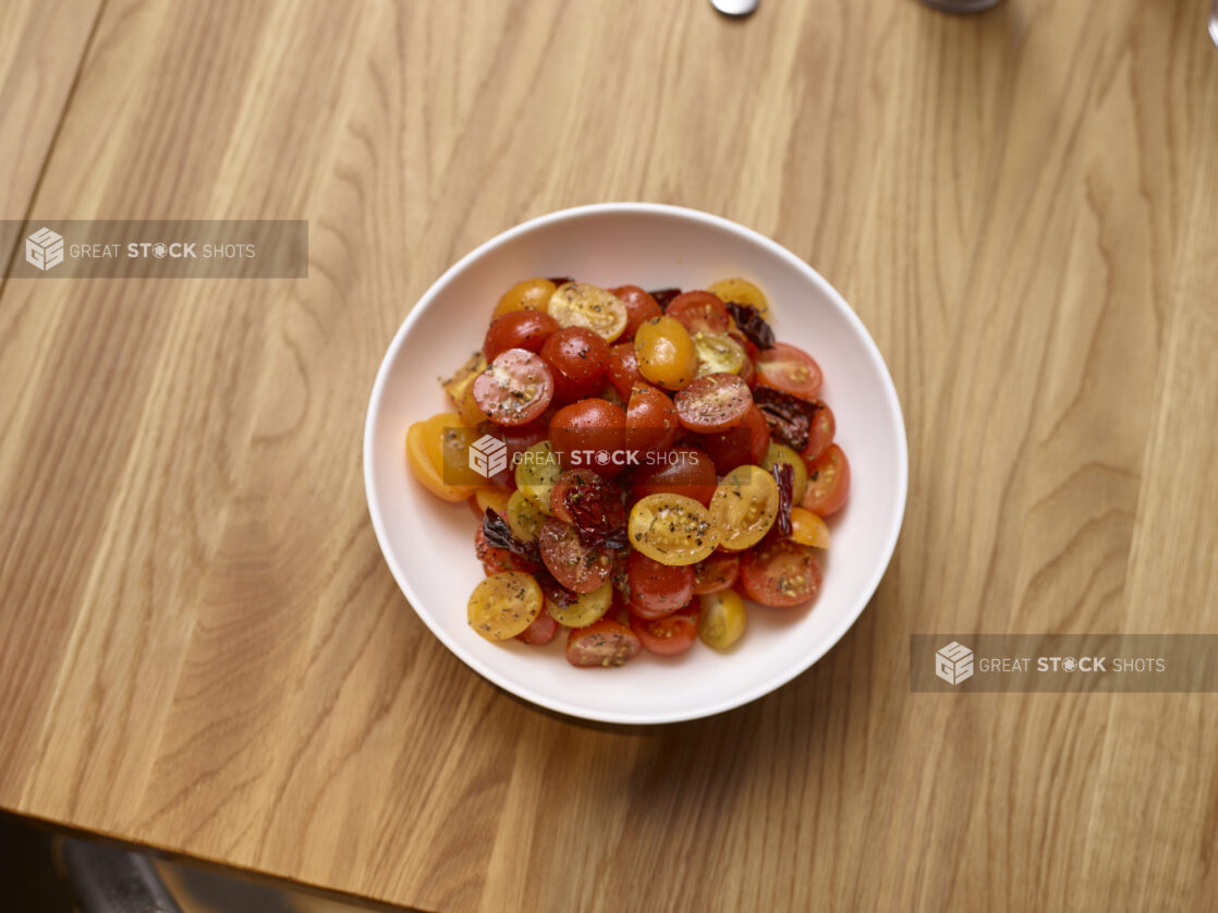 Red and Yellow Grape Tomato Salad with a Lemon Wedge in a Round White Ceramic Salad Bowl on a Wooden Table