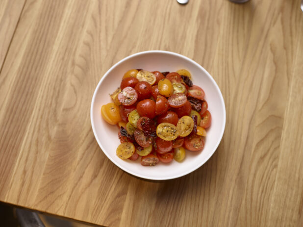Red and Yellow Grape Tomato Salad with a Lemon Wedge in a Round White Ceramic Salad Bowl on a Wooden Table